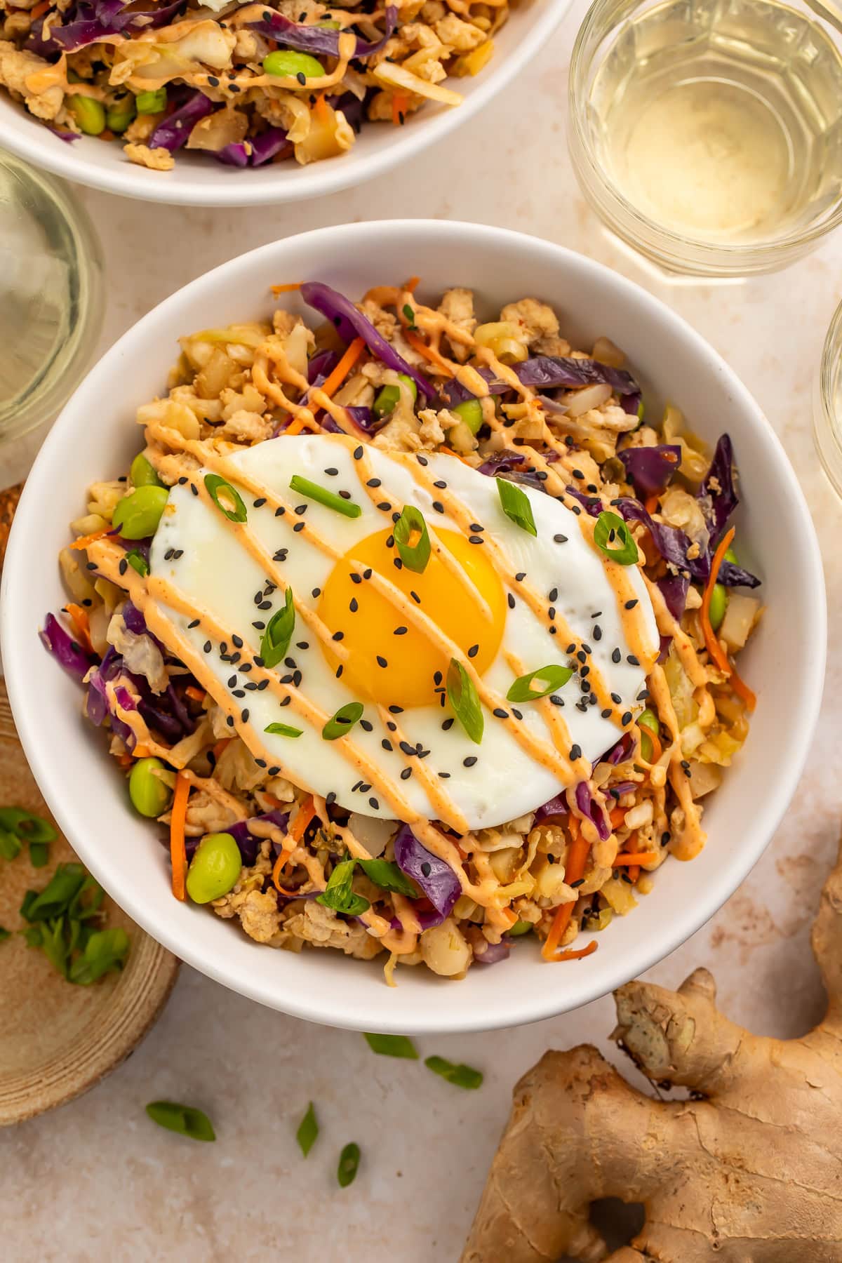 Close-up of egg roll in a bowl showing ground pork, purple cabbage, edamame, and fried egg with creamy sauce