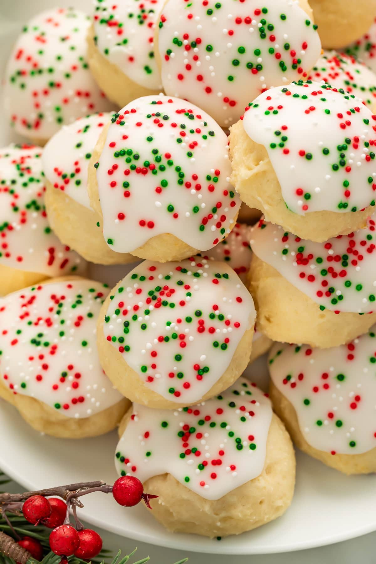 Italian Christmas cookies with almond glaze and holiday sprinkles piled on white plate with red berries