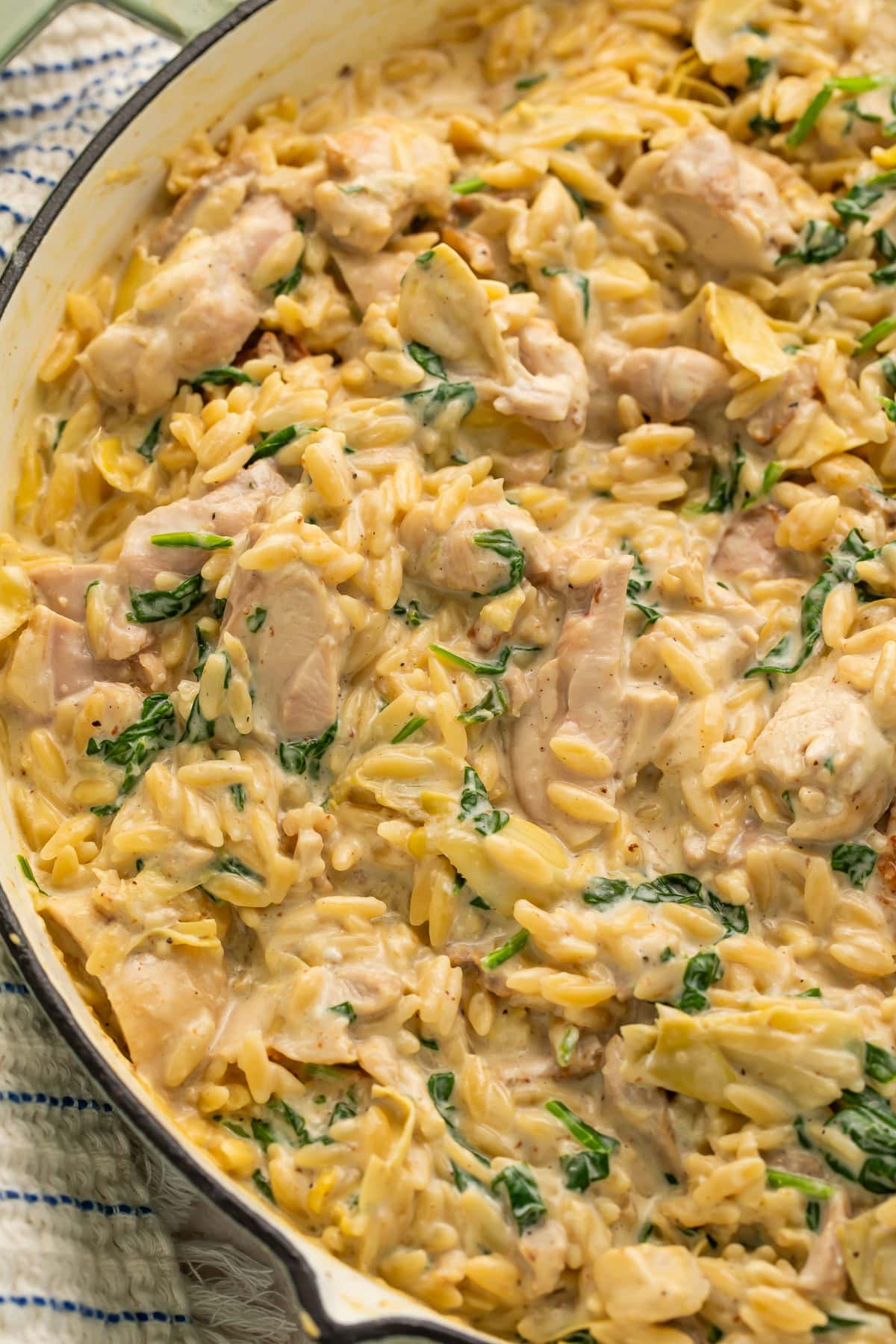 Overhead view of creamy chicken orzo with spinach, artichokes, and parmesan in white enameled skillet