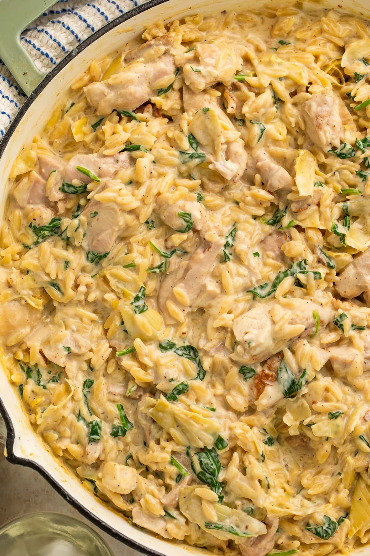 Creamy orzo pasta with chicken, spinach, and artichoke hearts in white skillet with melted Parmesan cheese