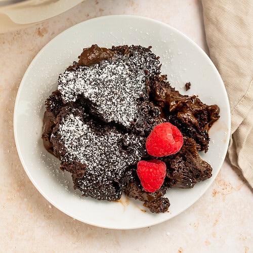 Slow cooker molten lava cake with powdered sugar and fresh raspberries on white plate