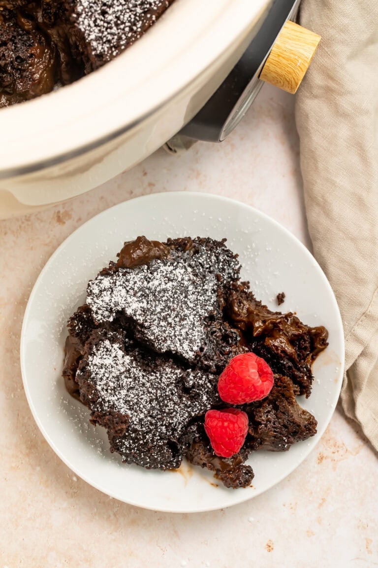 Slow cooker molten lava cake with powdered sugar and fresh raspberries on white plate