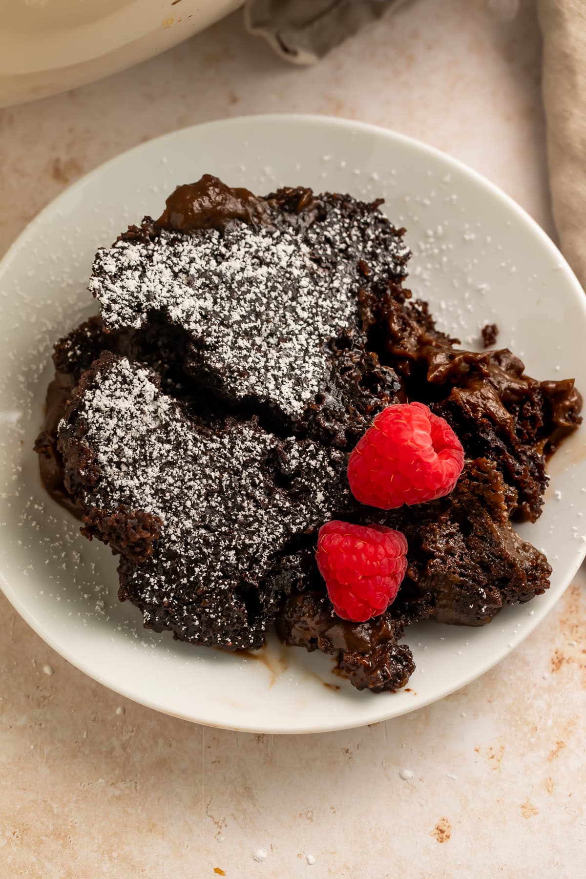 Close up of chocolate lava cake with powdered sugar and raspberries on white plate
