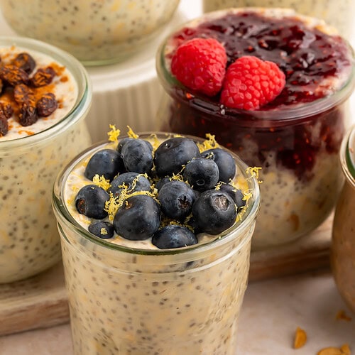 High protein overnight oats in glass jar topped with fresh blueberries and lemon zest on beige surface