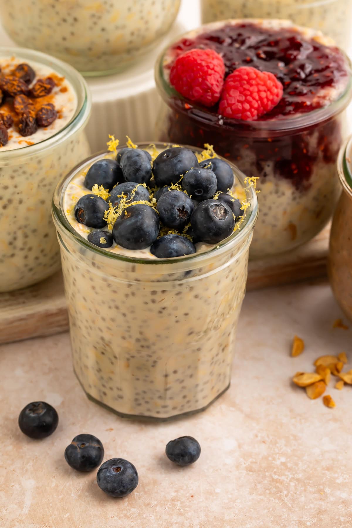 High protein overnight oats in glass jar topped with fresh blueberries and lemon zest on beige surface