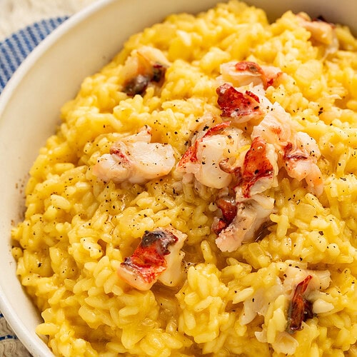 Creamy golden lobster risotto topped with butter-poached lobster chunks and black pepper in a white bowl