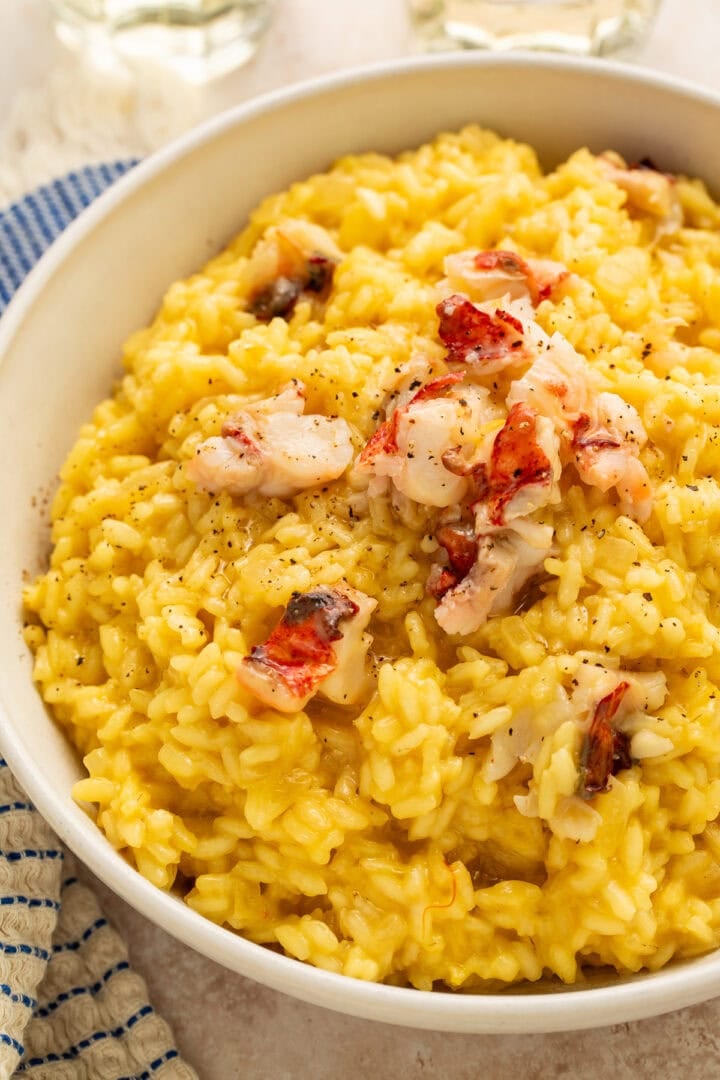 Creamy golden lobster risotto topped with butter-poached lobster chunks and black pepper in a white bowl
