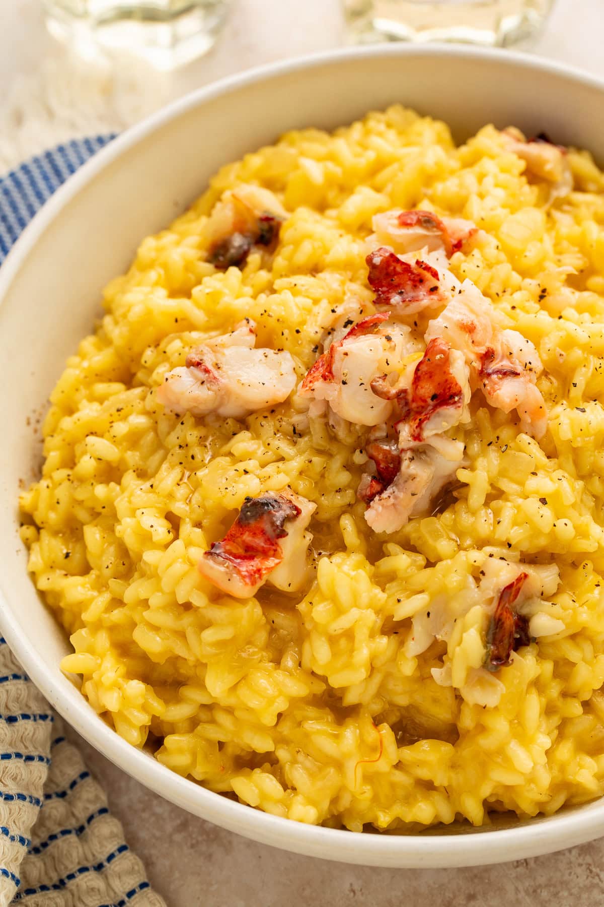 Creamy golden lobster risotto topped with butter-poached lobster chunks and black pepper in a white bowl