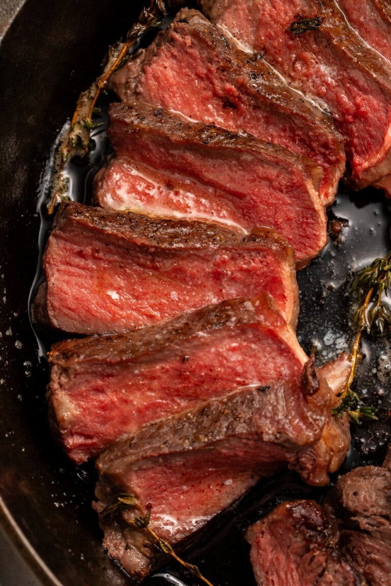 Sliced medium-rare ribeye steak with pink interior and dark seared crust in black cast iron skillet.