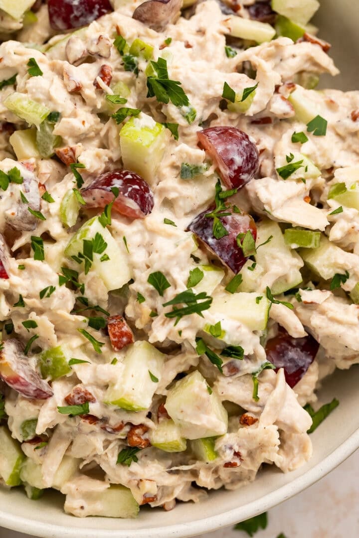 Close up view of high protein chicken salad with grapes, apples, pecans, and fresh parsley in white bowl
