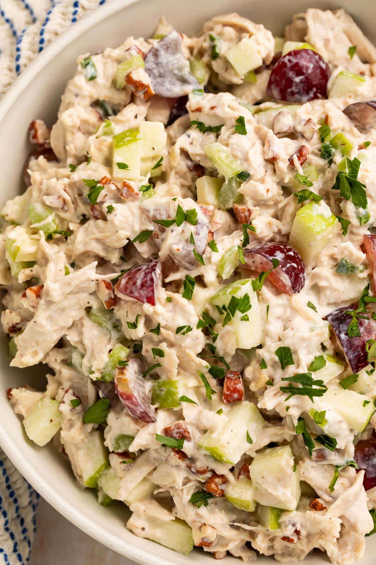 Overhead view of chicken salad in white bowl showing chunks of chicken, red grapes, apples, and pecans