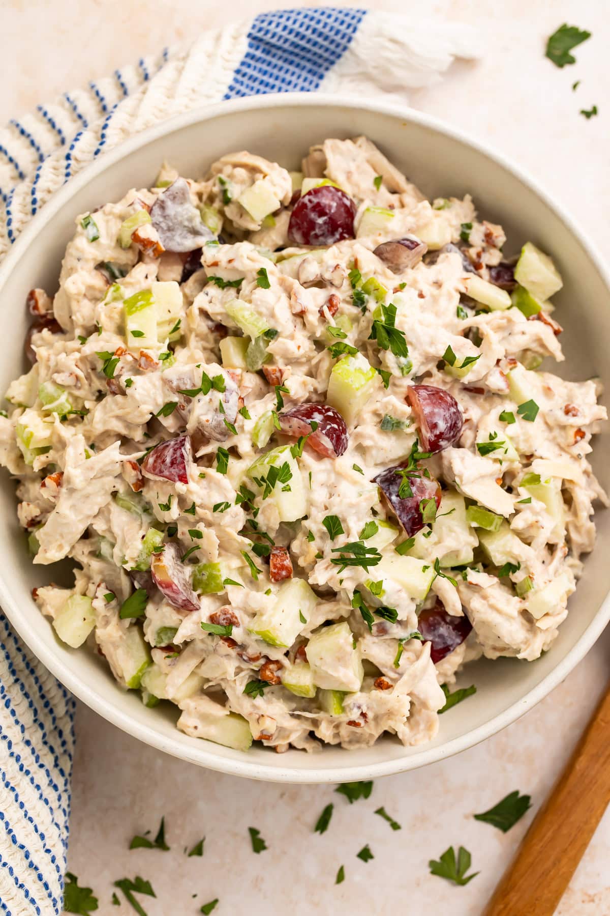 High protein chicken salad in white bowl on wooden surface with blue striped kitchen towel and fresh parsley