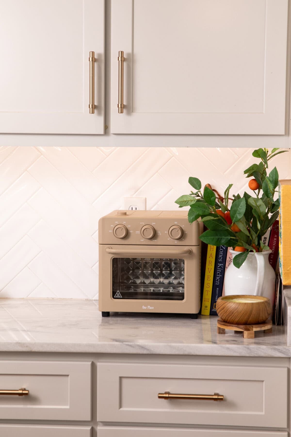 Beige Our Place air fryer oven on white kitchen counter with herringbone tile backsplash