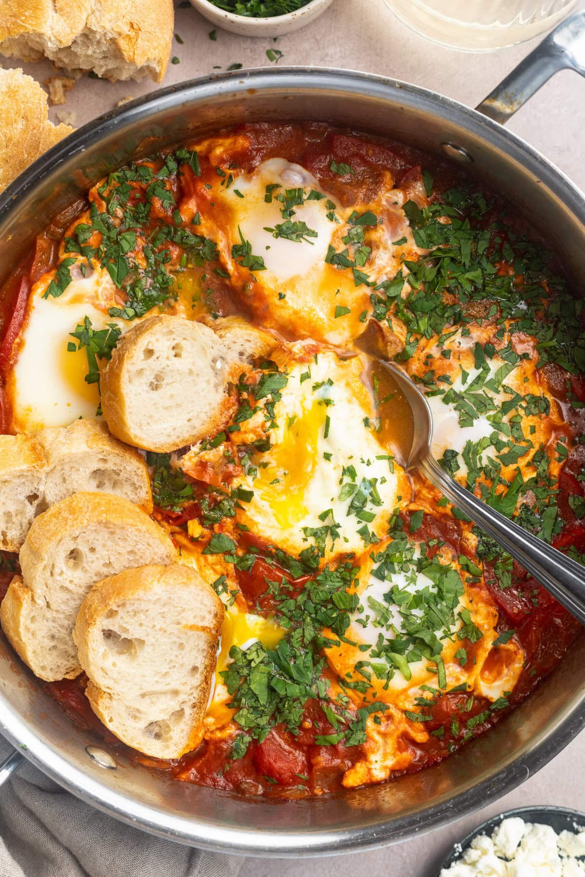 Overhead view of shakshuka with six poached eggs nestled in spiced tomato sauce, topped with chopped fresh herbs in a stainless steel skillet