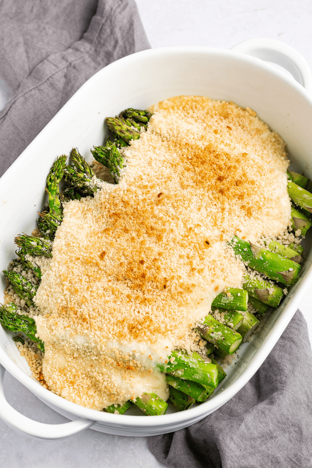 Overhead view of cheesy asparagus casserole in a white oval baking dish with golden crumb topping