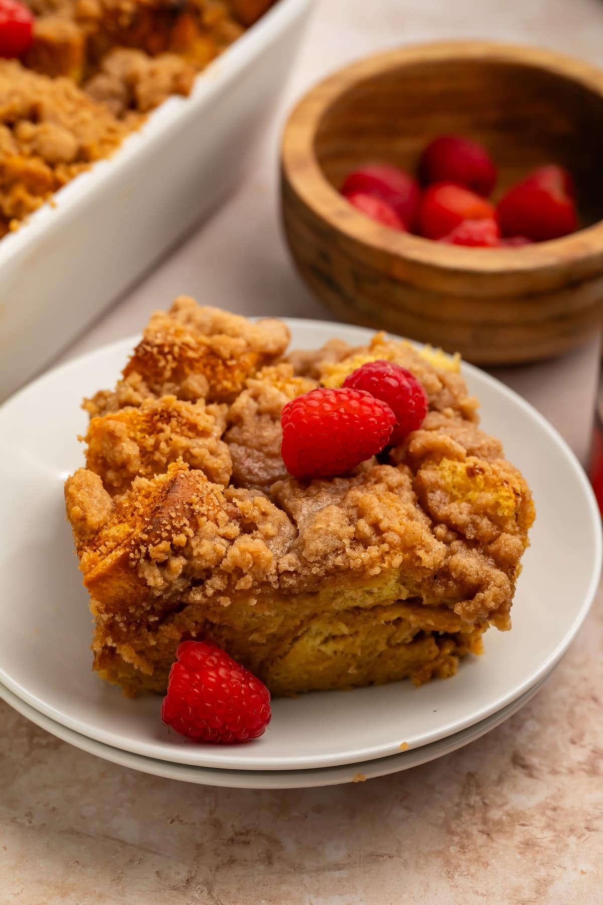 Close-up slice of brioche French toast casserole with streusel topping and fresh raspberries on a white plate 