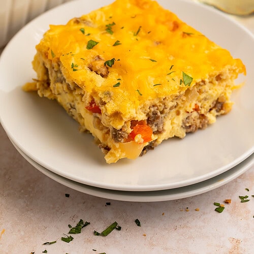 A square slice of cottage cheese egg bake with melted cheddar and parsley on a white plate