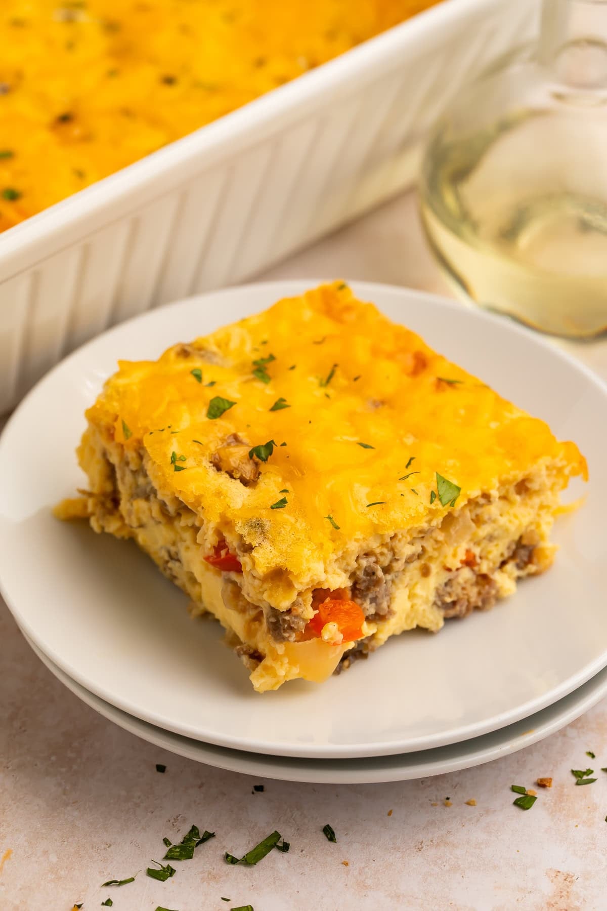 A square slice of cottage cheese egg bake with melted cheddar and parsley on a white plate