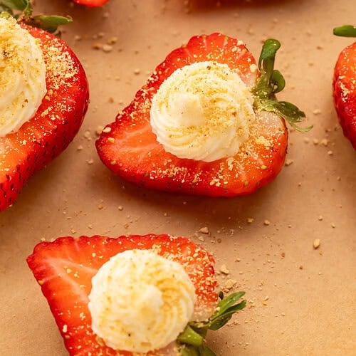 Close-up of deviled strawberries with piped cream cheese filling and graham cracker crumbs on parchment paper
