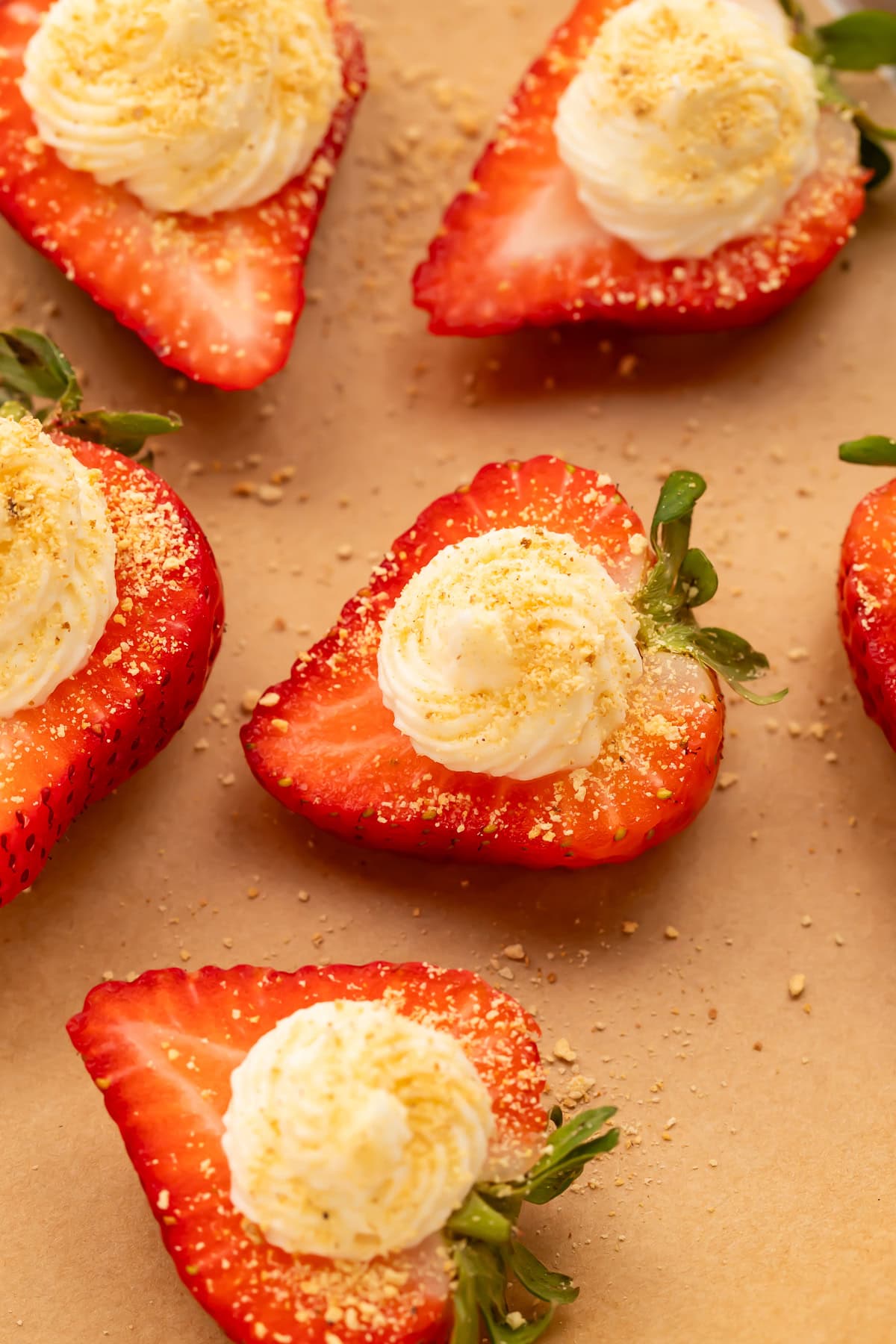 Close-up of deviled strawberries with piped cream cheese filling and graham cracker crumbs on parchment paper