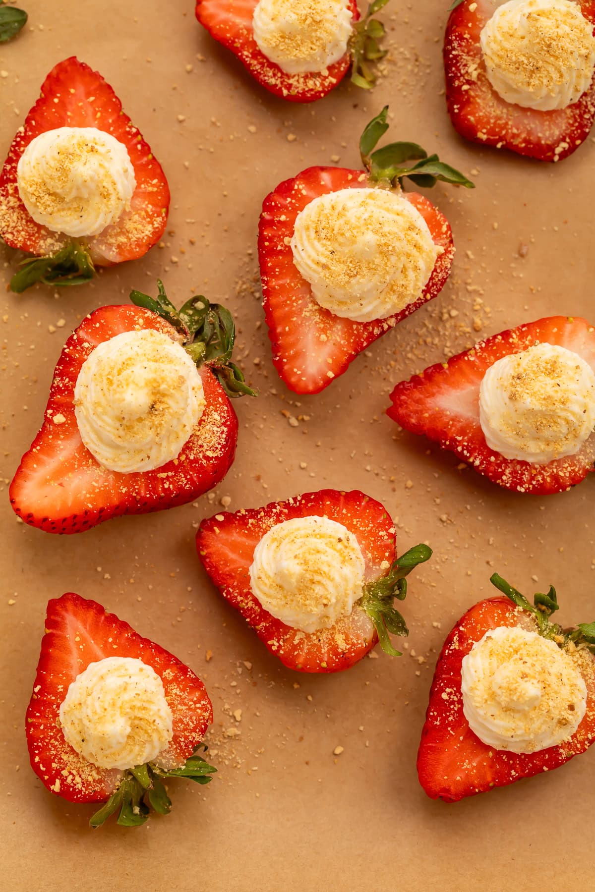 Deviled strawberries with whipped cream cheese filling and graham cracker crumbs on parchment paper