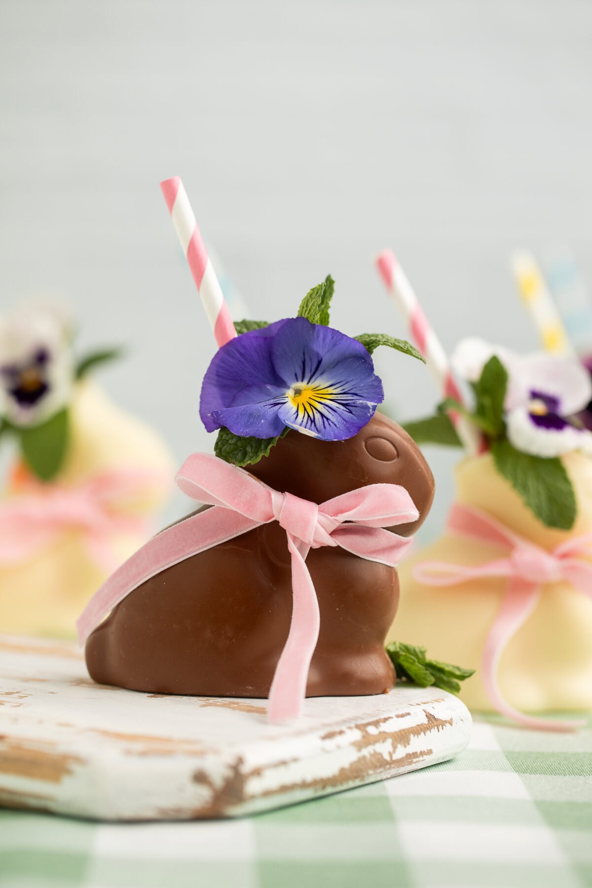 A hollow chocolate bunny filled with a cocktail, garnished with a purple pansy, fresh mint, and a pink striped straw.