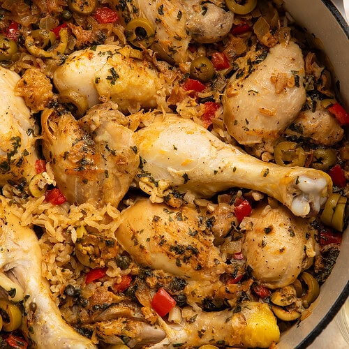 One pot Spanish chicken and rice with drumsticks, green olives, red pepper, and herbs in a Dutch oven
