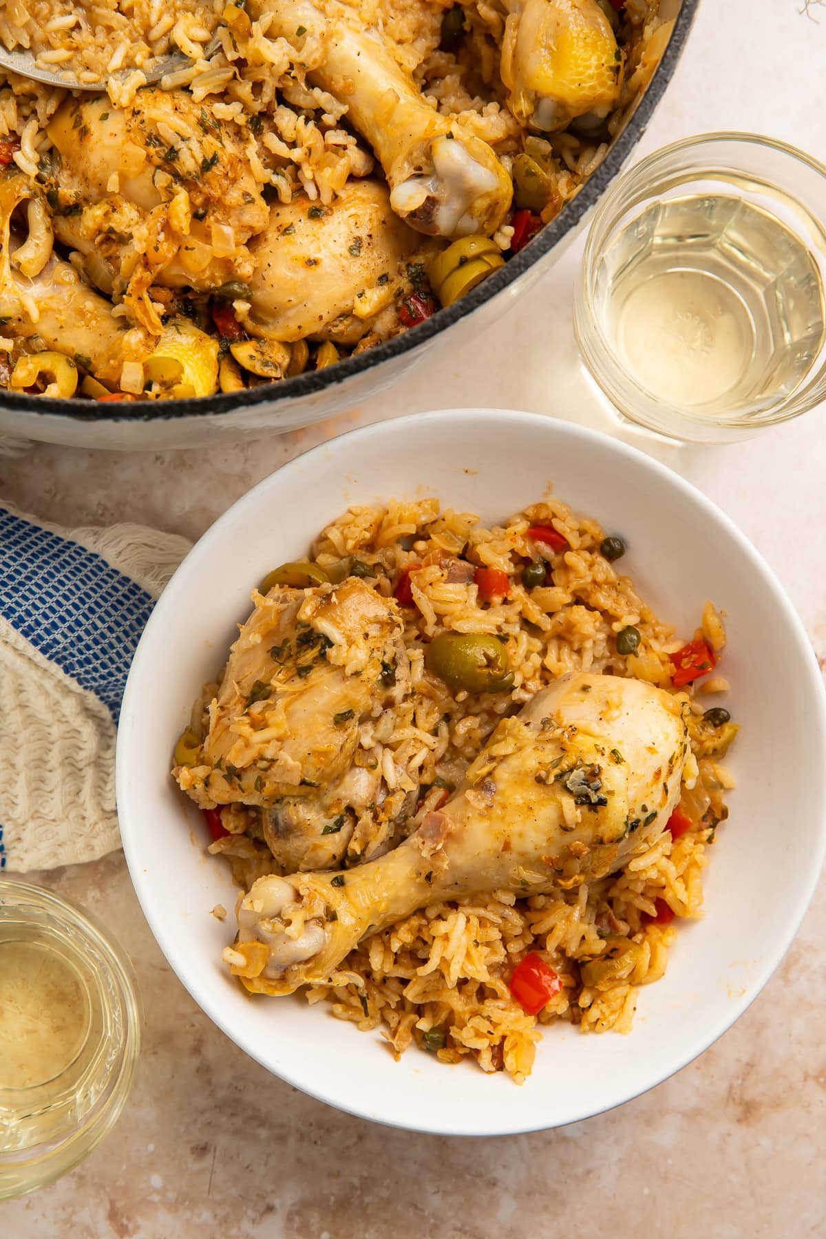 White bowl of Spanish chicken and rice with a drumstick, green olives, capers, and red pepper pieces