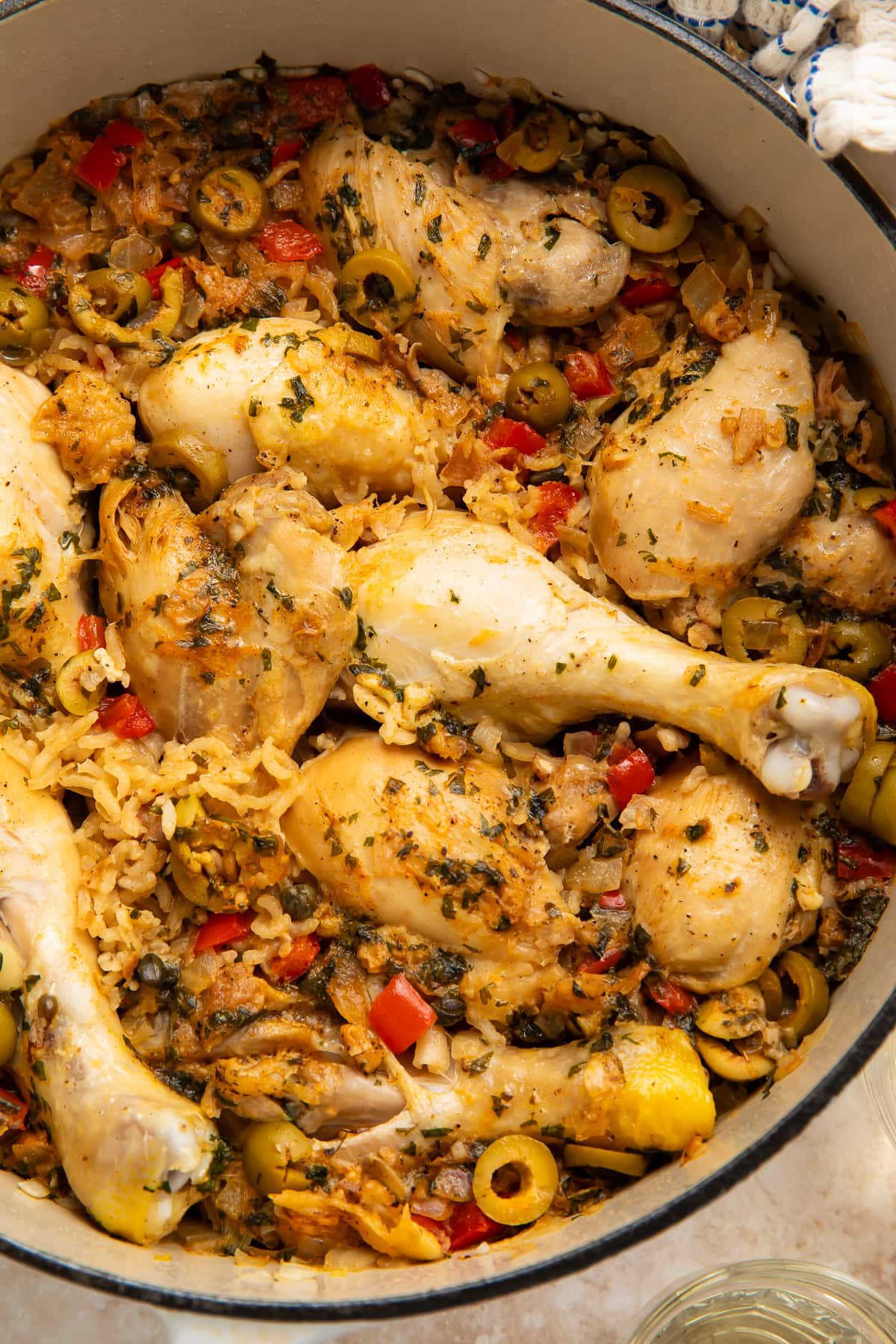Close-up overhead of chicken drumsticks in seasoned rice with green olives, capers, red pepper, and fresh herbs