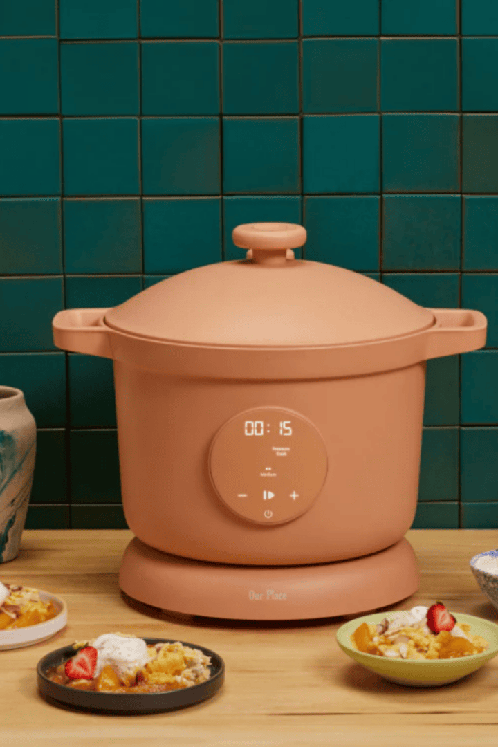 Our Place Dream Cooker in terracotta on a wood surface surrounded by bowls of food