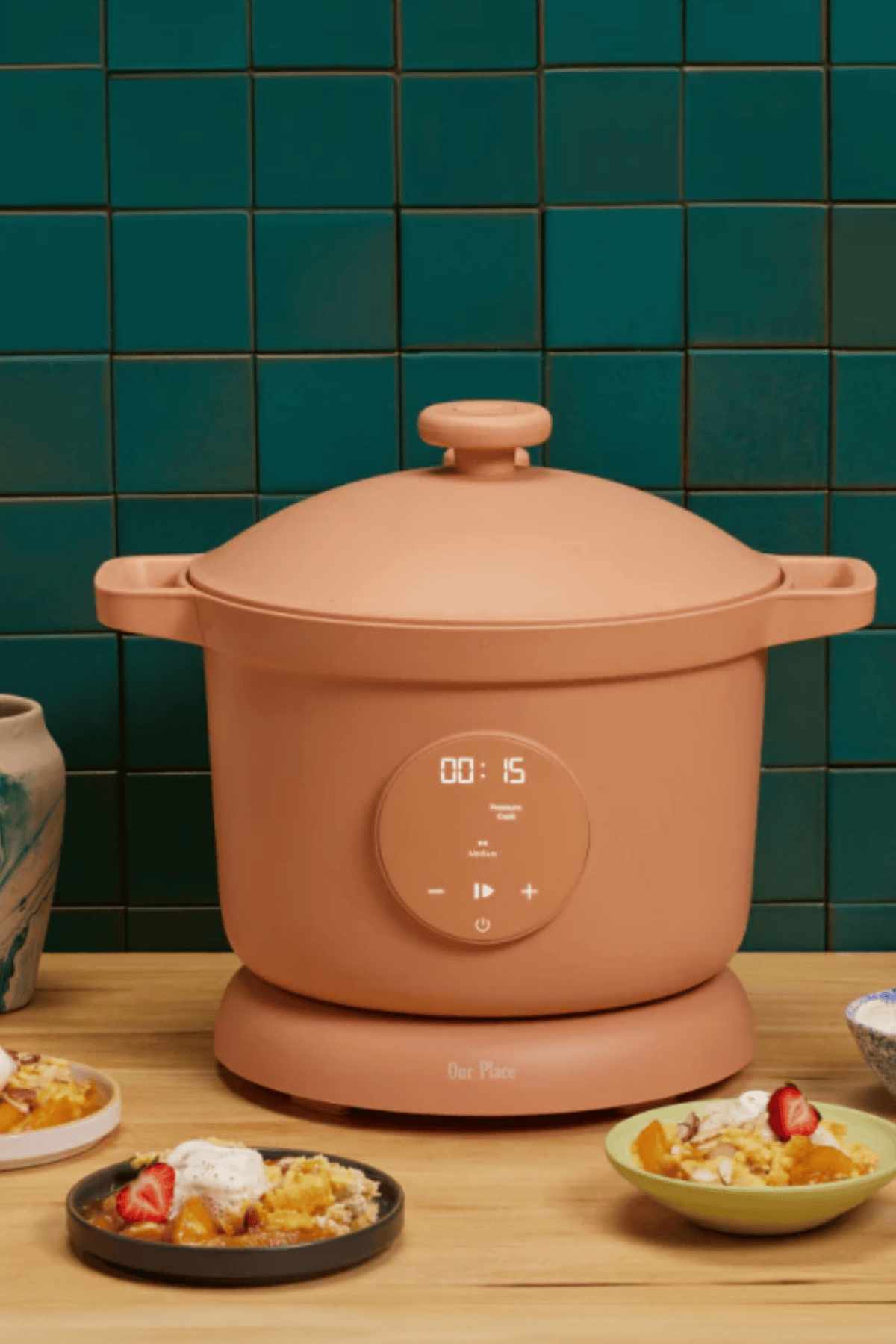 Our Place Dream Cooker in terracotta on a wood surface surrounded by bowls of food