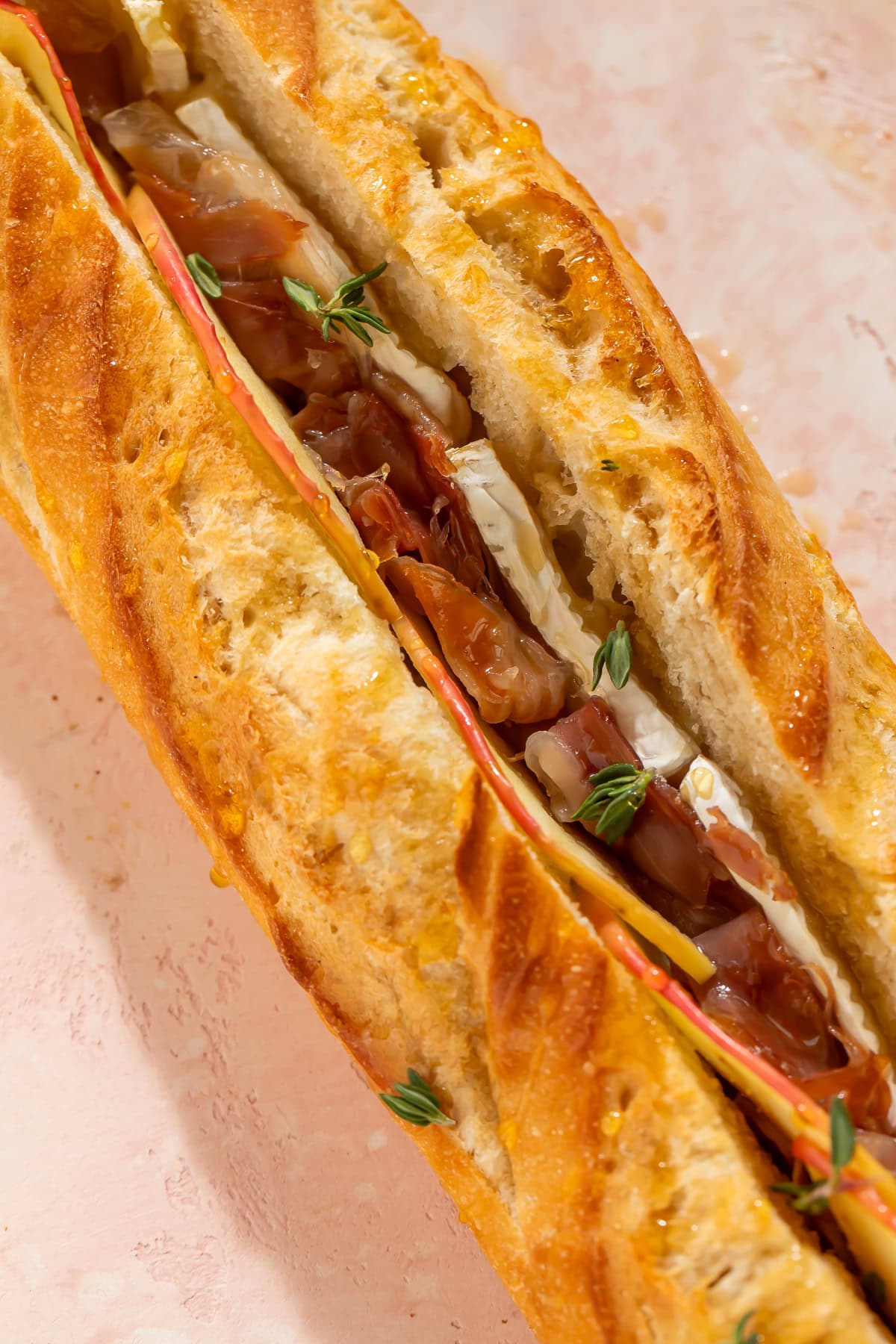Close-up of a baked brie and prosciutto stuffed baguette showing melted brie, prosciutto, apple slices, and thyme
