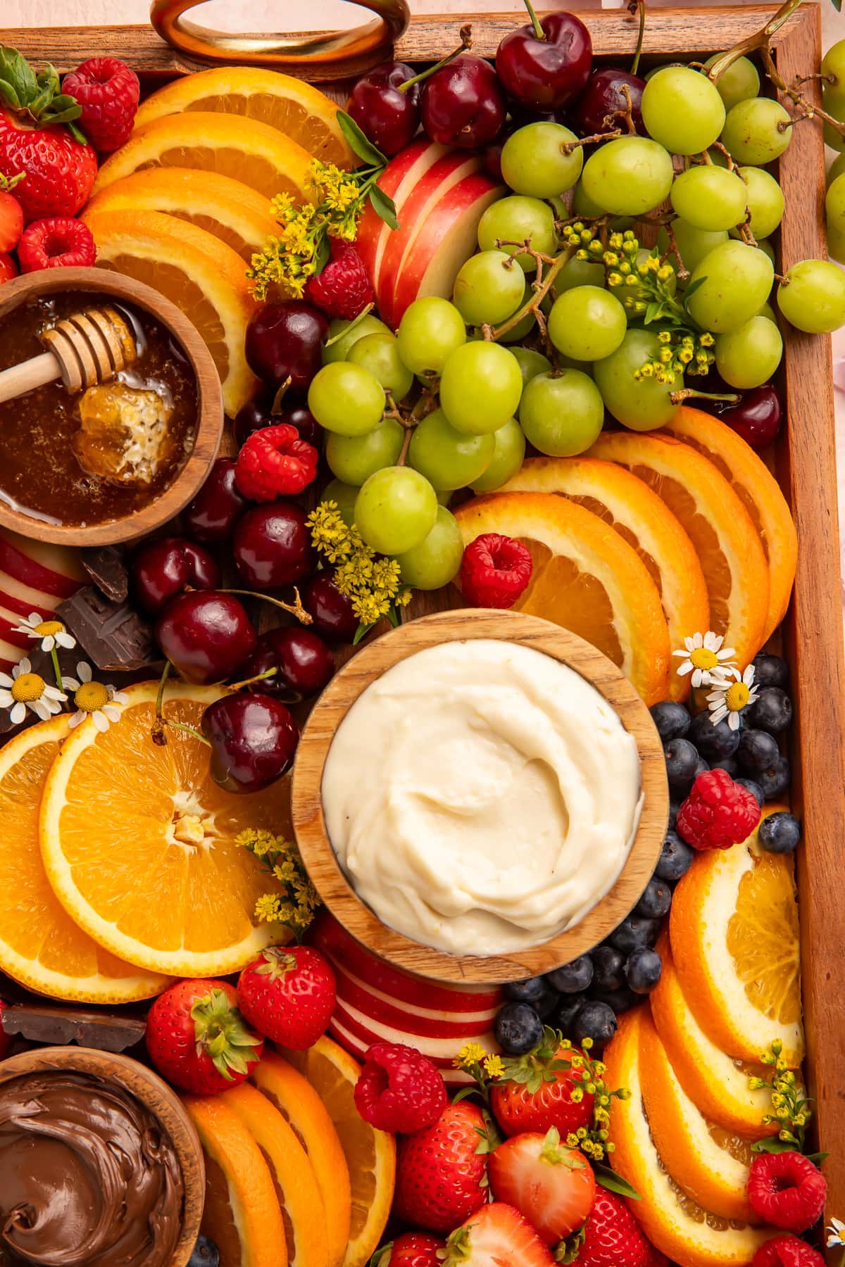 Overhead close-up of a fruit board with orange slices, cherries, green grapes, berries, and cream cheese dip