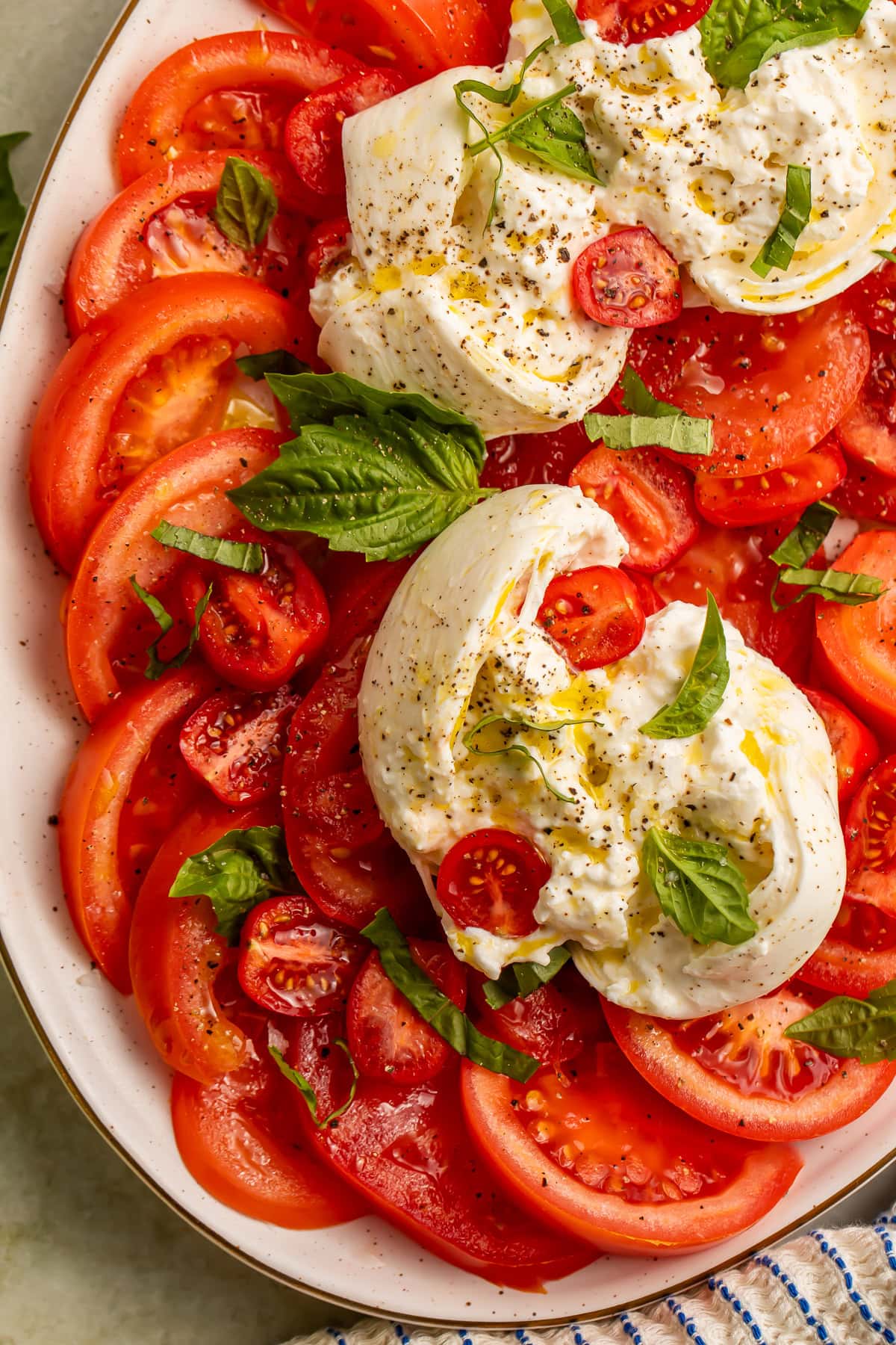Close-up of burrata caprese salad with sliced tomatoes, fresh basil, and olive oil on a platter