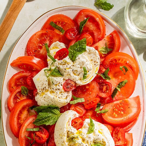 Overhead view of full burrata caprese salad platter with tomatoes, burrata, and chiffonaded basil
