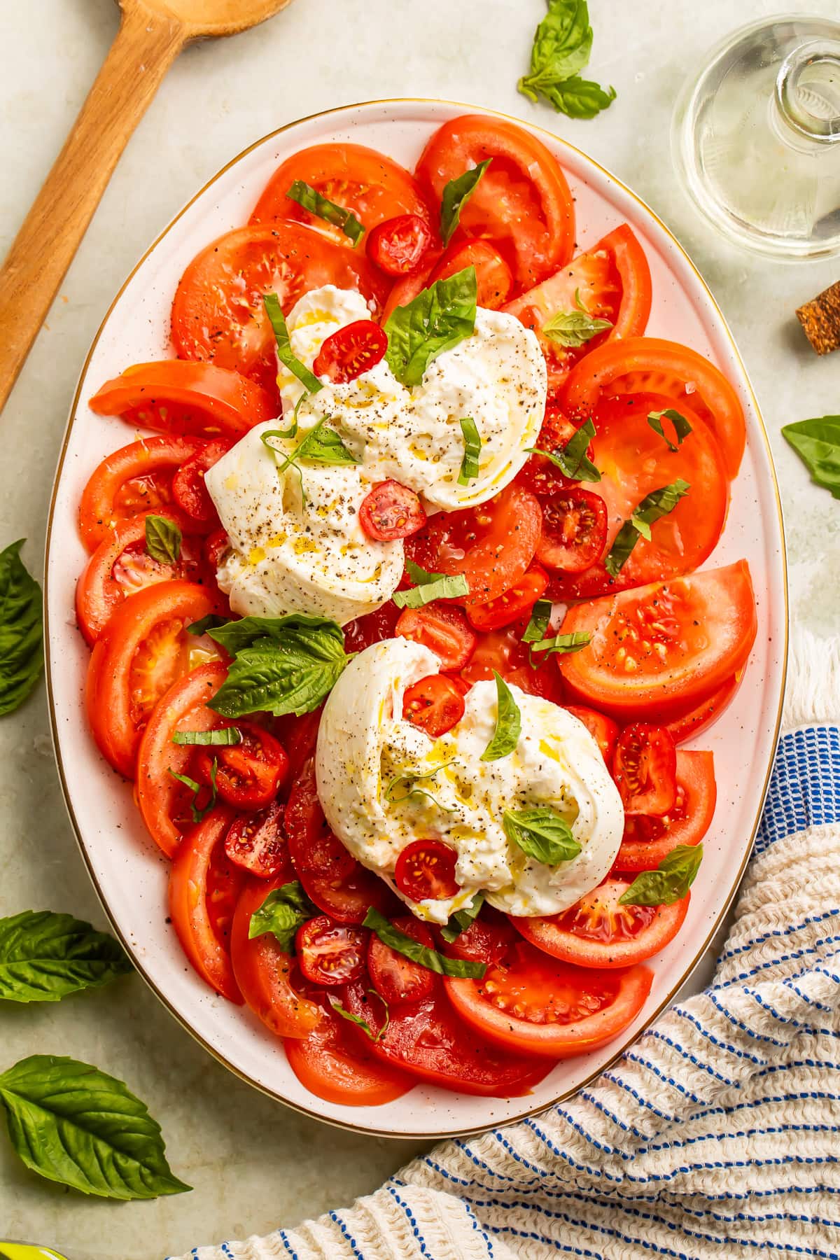 Full overhead view of burrata caprese salad on an oval gold-rimmed platter with tomatoes and basil