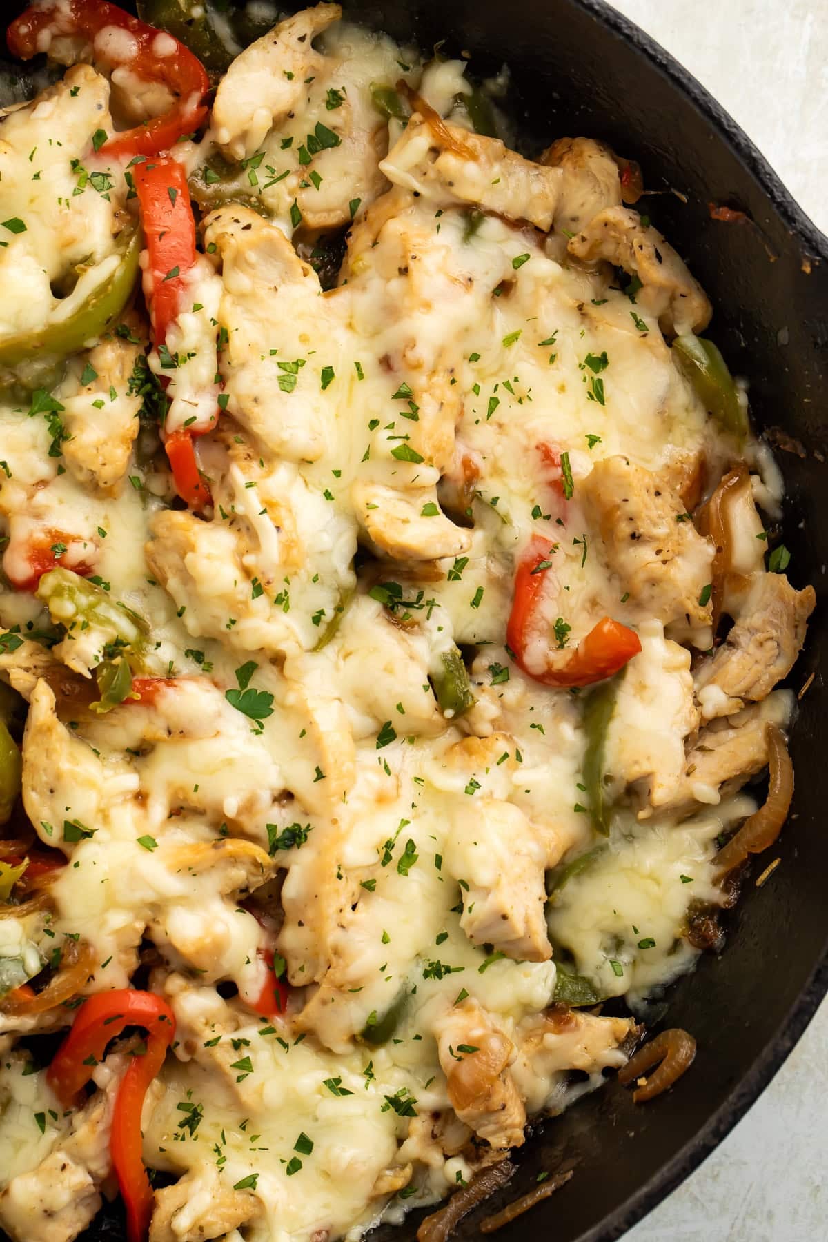 Close-up of chicken Philly cheesesteak skillet with melted provolone, red and green bell peppers, and fresh parsley