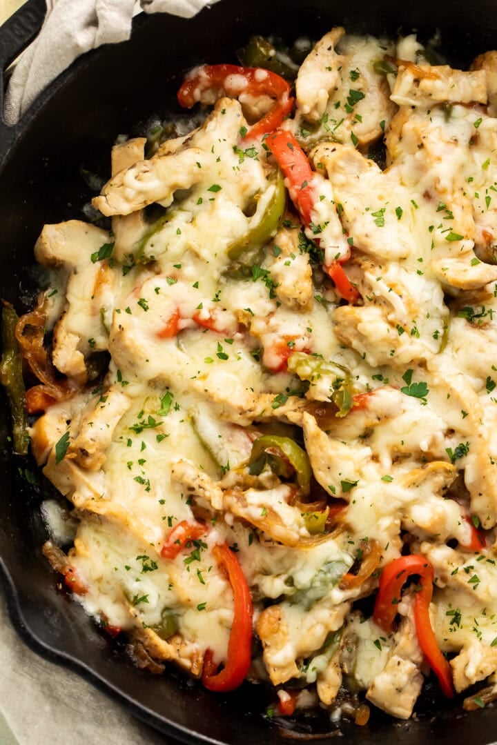 Cast iron skillet filled with chicken Philly cheesesteak, melted cheese, colorful peppers, and fresh parsley garnish
