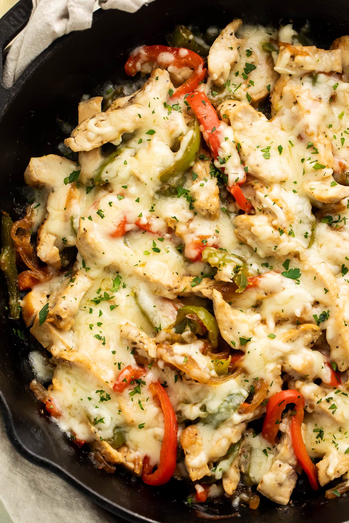Cast iron skillet filled with chicken Philly cheesesteak, melted cheese, colorful peppers, and fresh parsley garnish