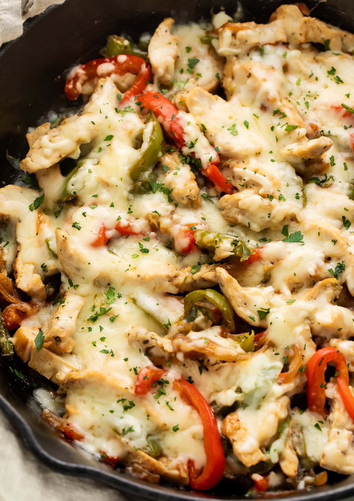 Angled view of chicken Philly cheesesteak in cast iron skillet with melted provolone and sautéed red and green peppers