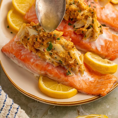 Overhead view of four baked crab stuffed salmon fillets on an oval cream plate with lemon slices