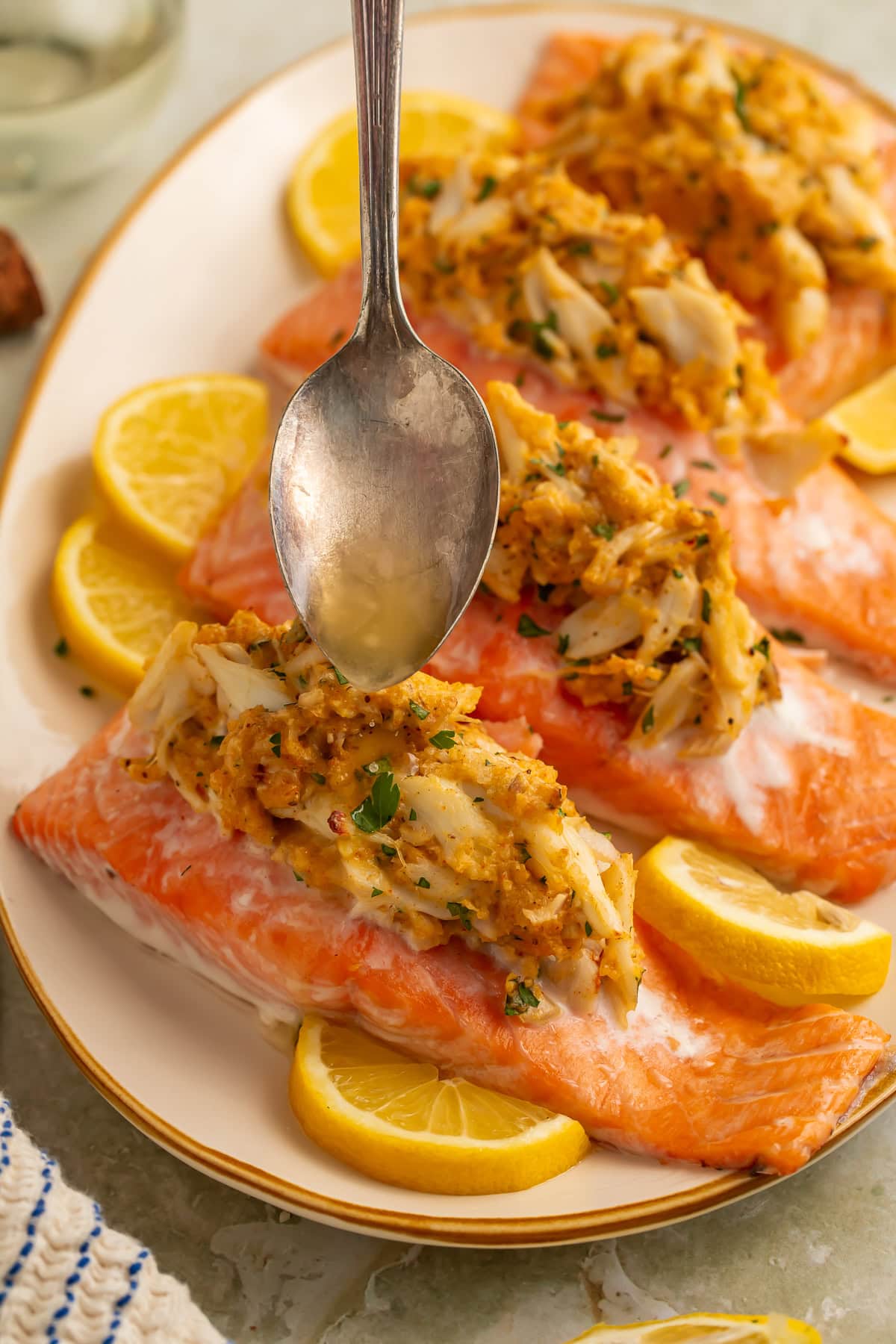 Overhead view of four baked crab stuffed salmon fillets on an oval cream plate with lemon slices