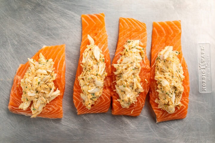 Crab stuffed salmon fillets lined up on a cutting board.