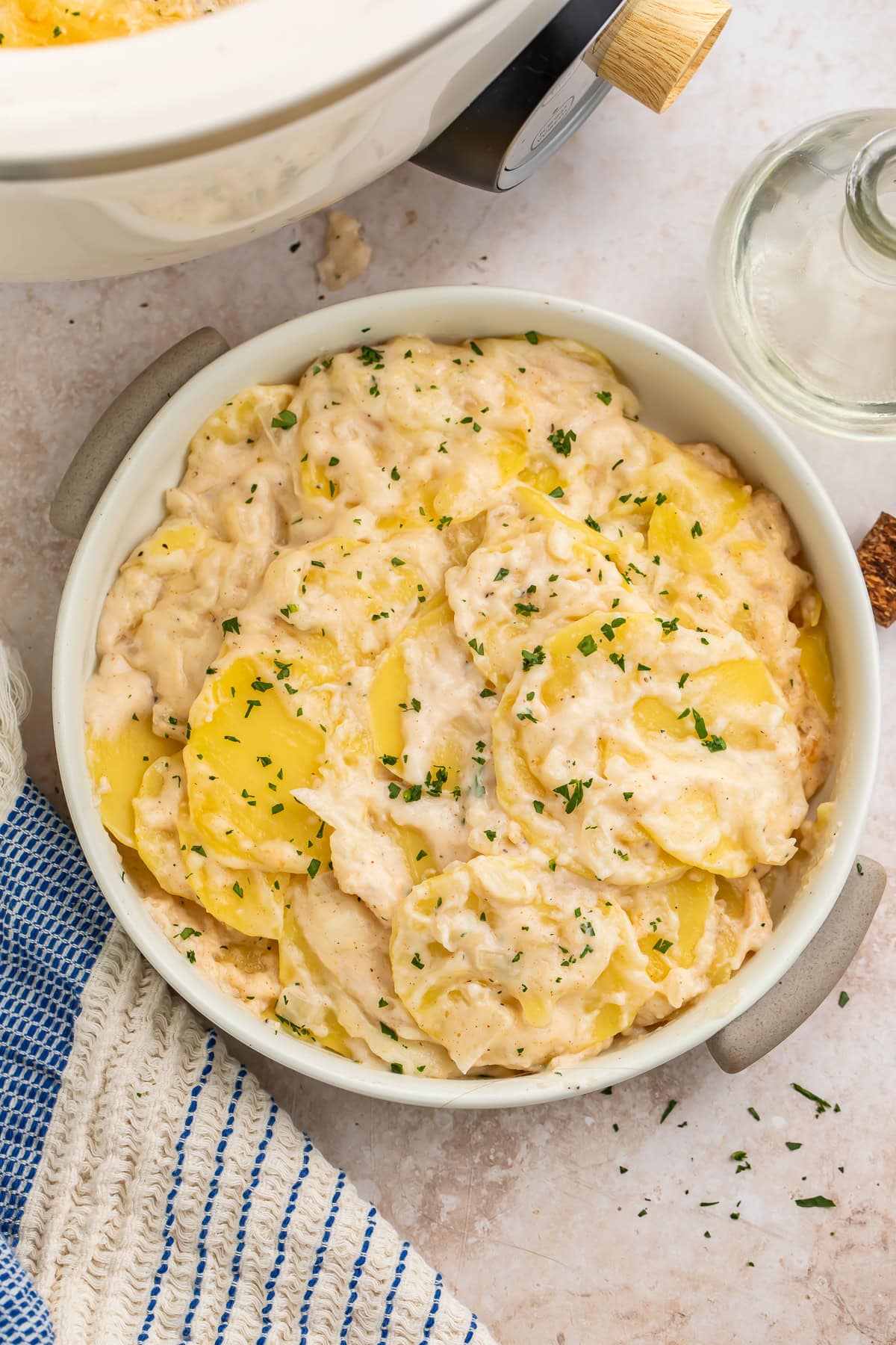 Crockpot scalloped potatoes in a round white serving dish garnished with fresh parsley