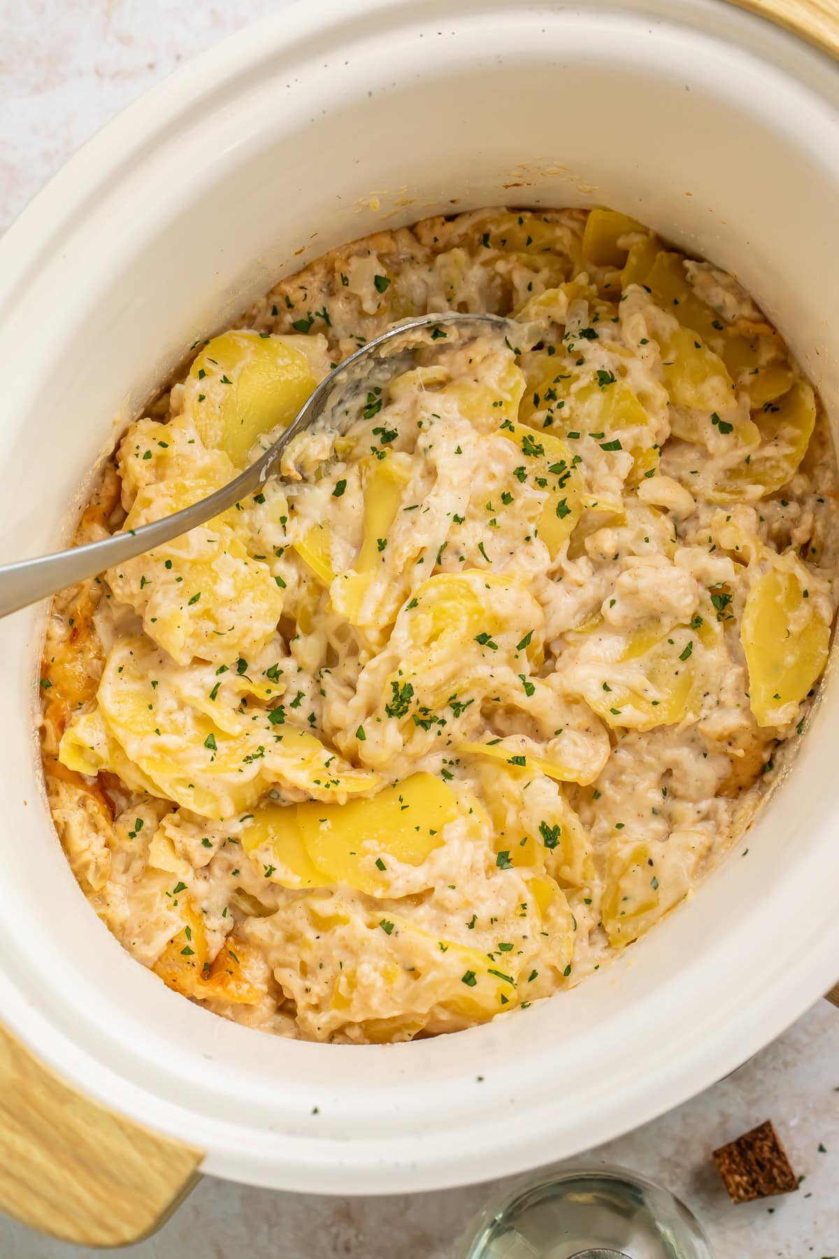 Overhead view of crockpot scalloped potatoes in a white slow cooker insert with a serving spoon