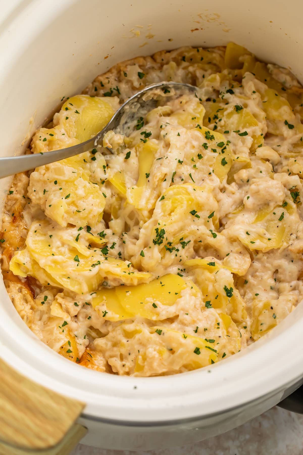Close-up of crockpot scalloped potatoes being scooped with a spoon, showing creamy layered potato slices
