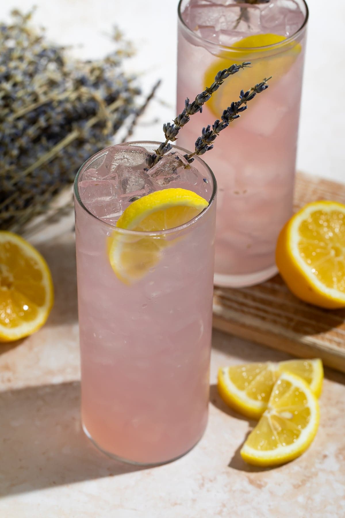 Two lavender lemonade cocktails in highball glasses garnished with lemon wedges and dried lavender sprigs