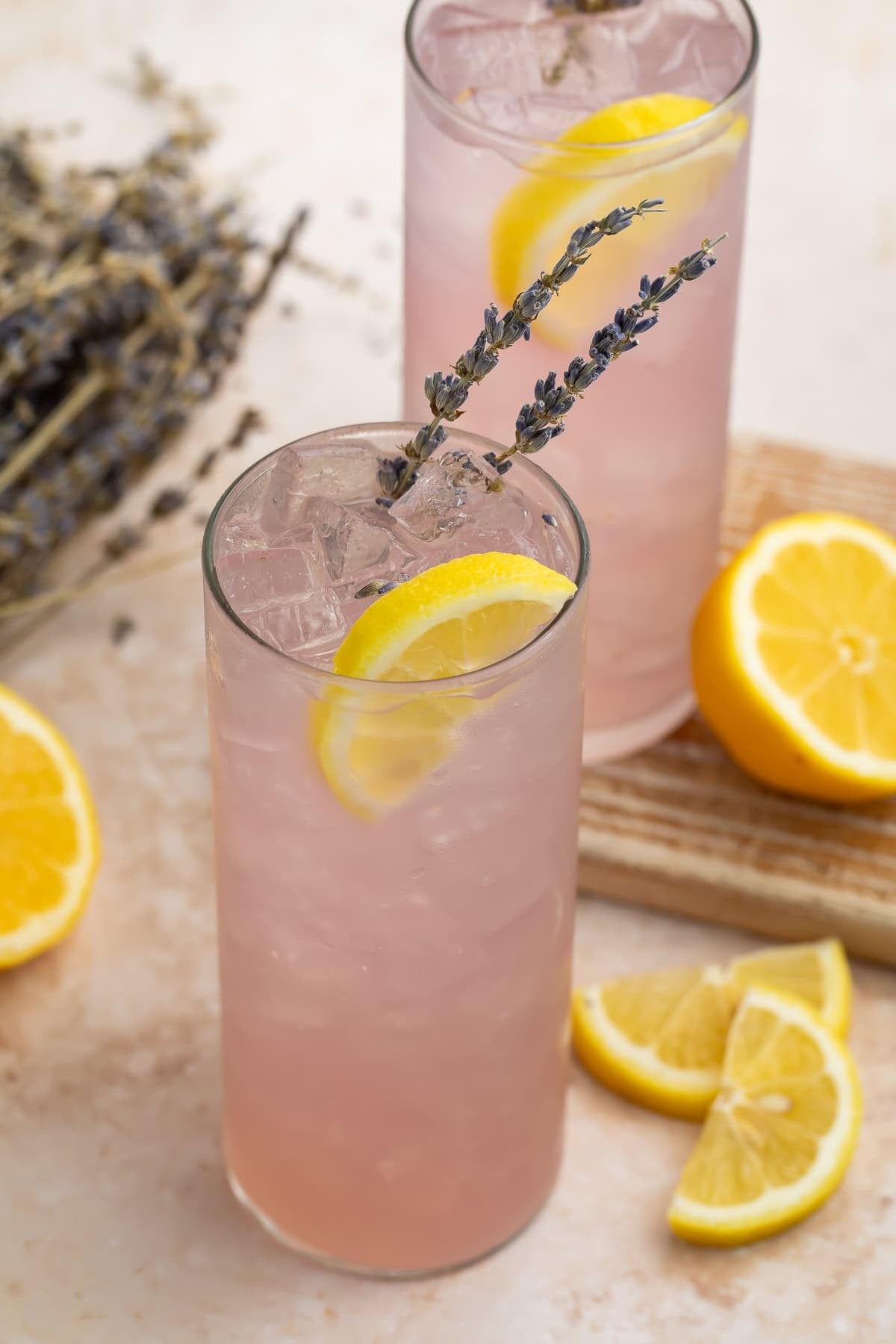 Close-up of two pink lavender lemonade cocktails over ice with lemon and lavender garnishes
