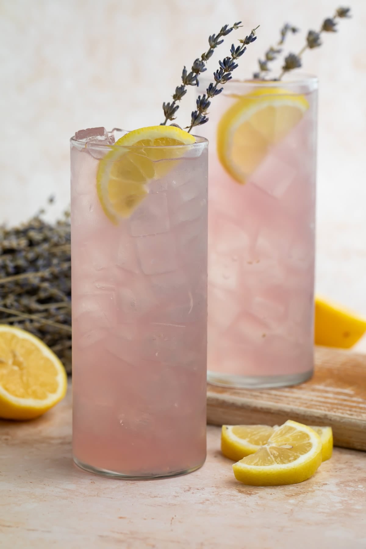 Two tall glasses of pale pink lavender lemonade cocktail with lemon slices and lavender garnish