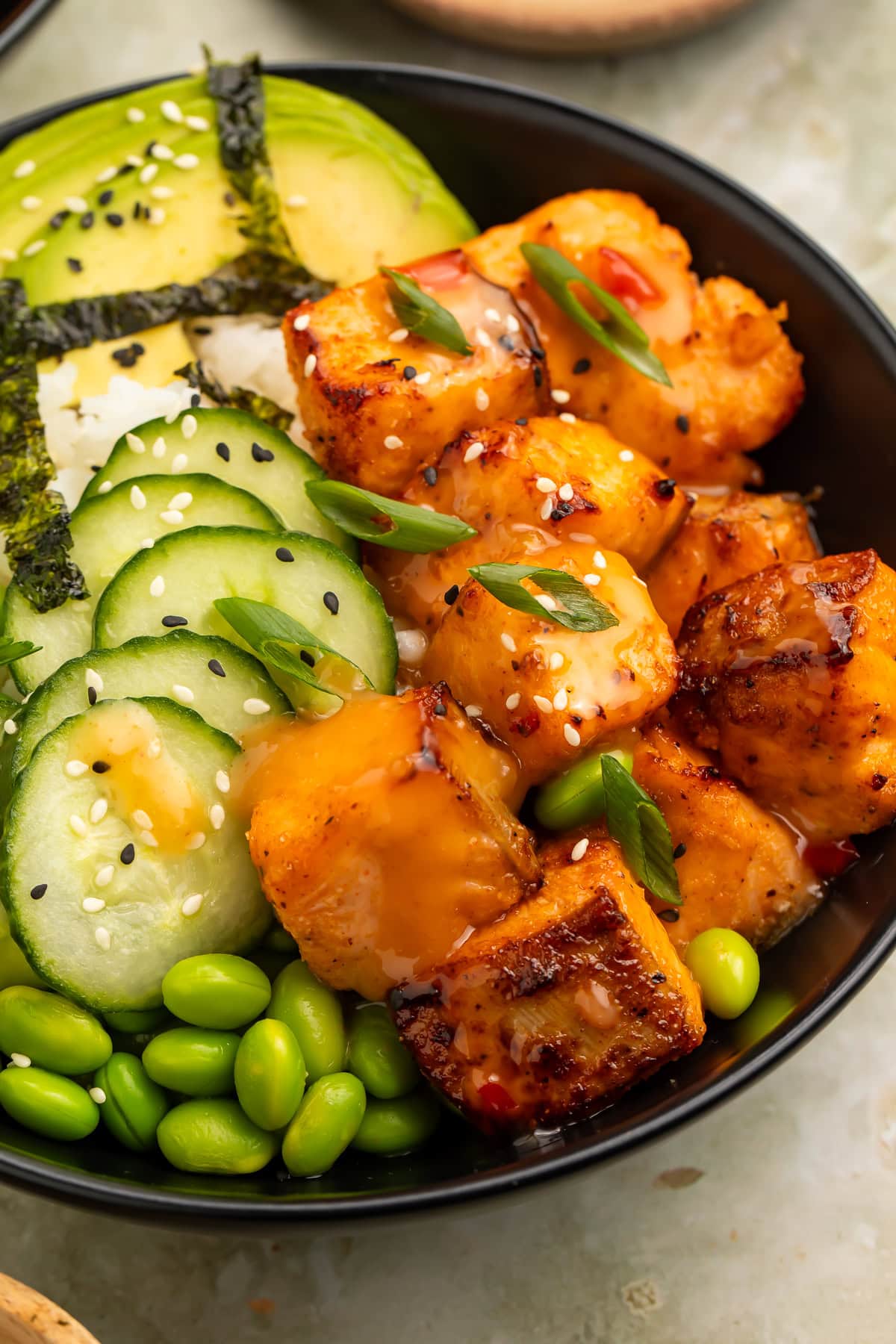 Bang bang salmon rice bowl with avocado, cucumber, edamame, seaweed, and glazed salmon bites topped with sesame seeds